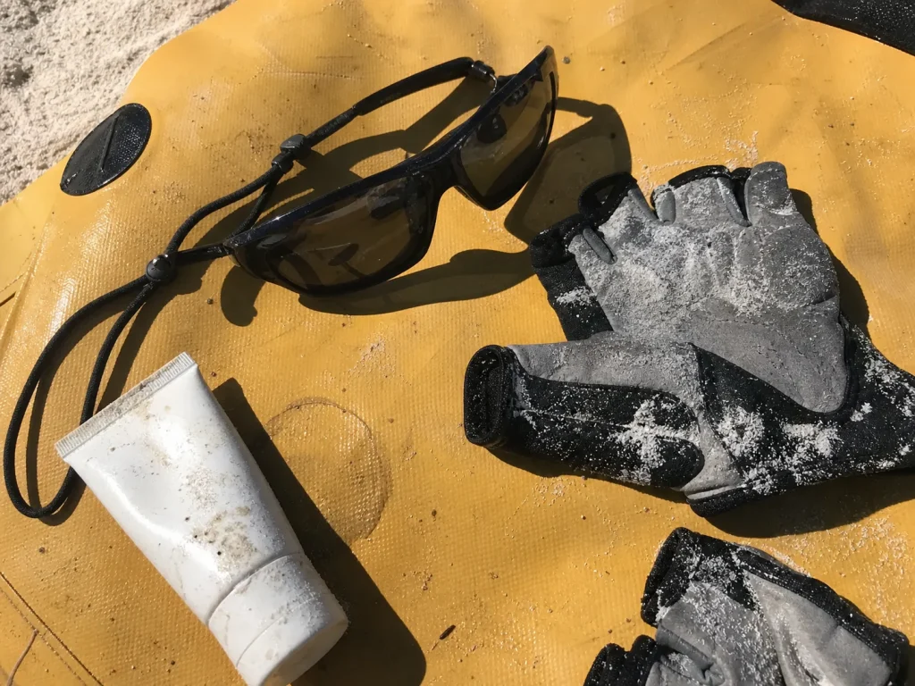 Polarized sunglasses paddling gloves and mineral sunscreen laid out on a dry bag