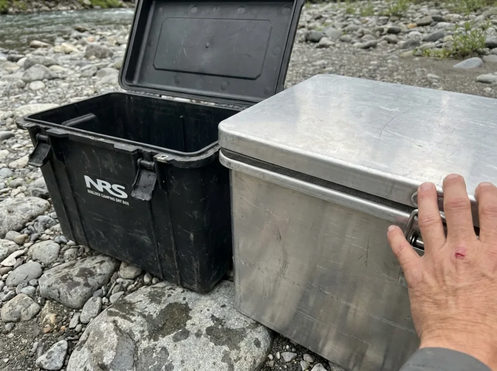 Rotomolded NRS dry box next to a welded aluminum box on wet river rock