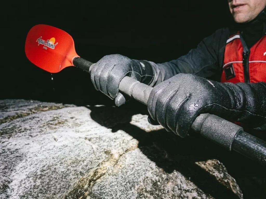 Cold wet gloved hands gripping a composite paddle shaft on a frigid early-season river morning