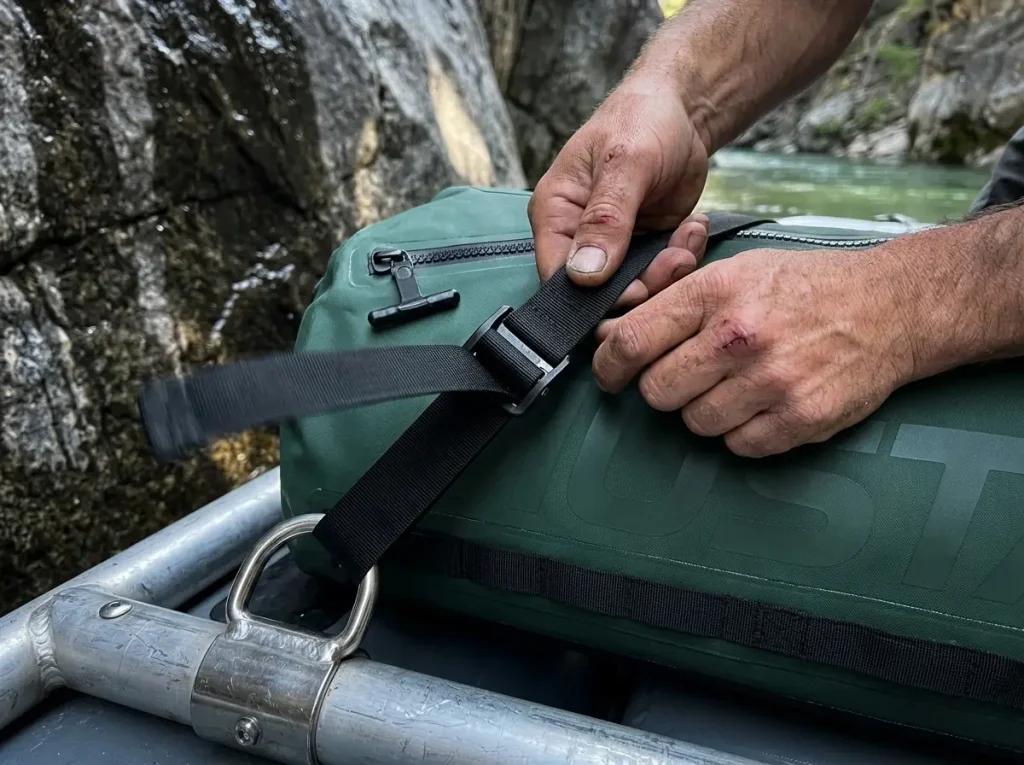 Close-up of a cam strap girth-hitched to a raft frame D-ring securing a dry bag