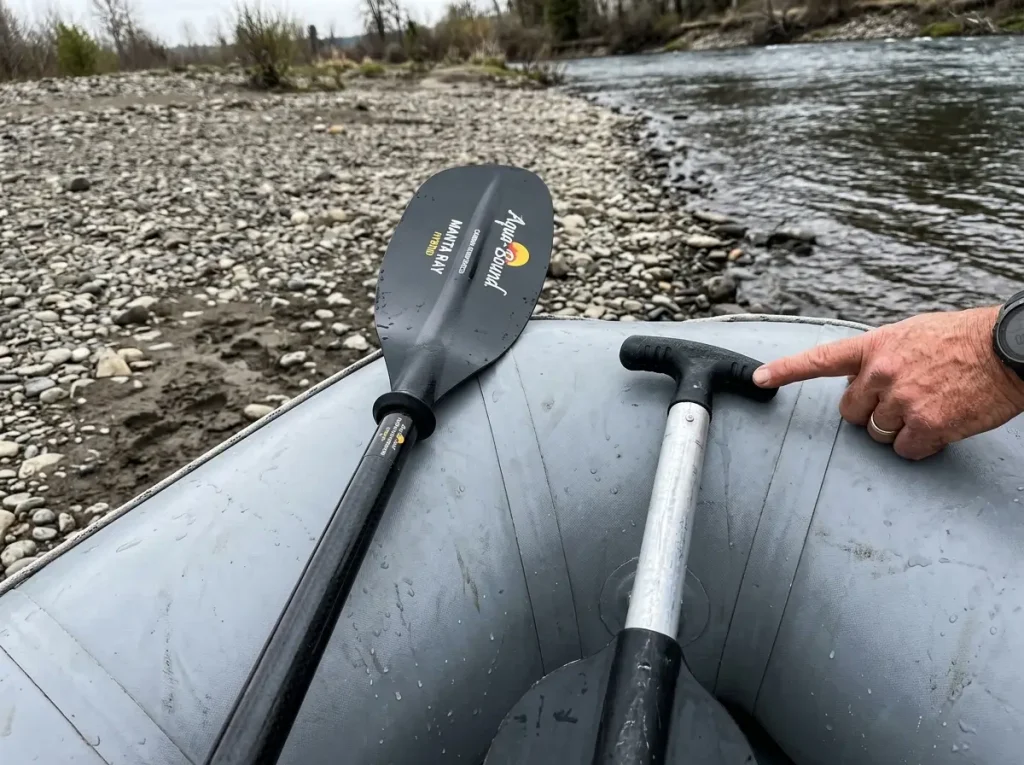 Double-blade kayak paddle and single-blade T-grip raft paddle laid side by side on a raft tube for comparison