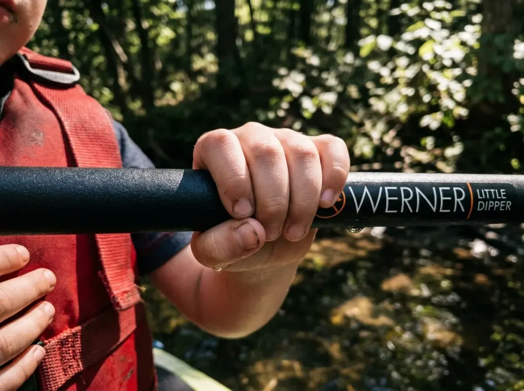 Close-up of a child's small hand fully wrapping a small-diameter kids paddle shaft showing proper grip
