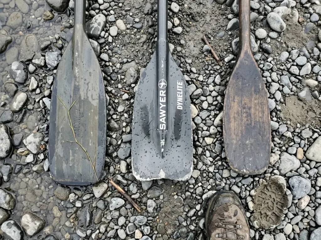 Different oar blade shapes including a Sawyer shoal-cut blade laid out on river gravel