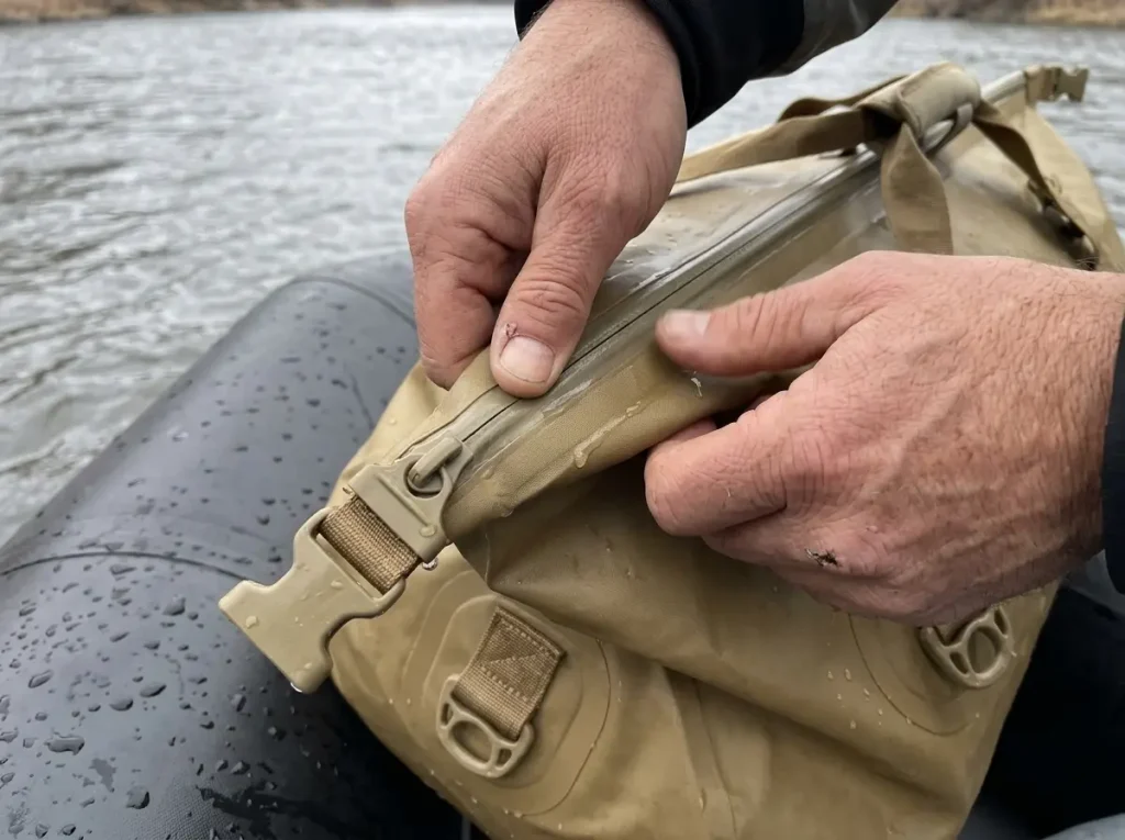 Hands sealing the ZipDry closure on a Watershed whitewater dry bag on a raft tube