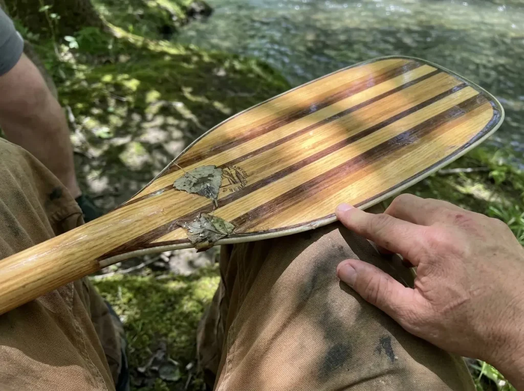 Close-up of a whitewater wood paddle blade with a fiberglass-wrapped edge showing hybrid construction