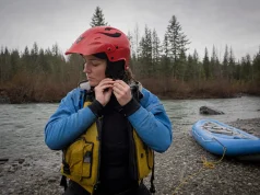 How to Choose a Whitewater Helmet That Won’t Ride Up Rafter adjusting the chinstrap of a full-cut whitewater helmet at a river put-in