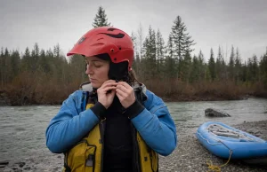 How to Choose a Whitewater Helmet That Won’t Ride Up Rafter adjusting the chinstrap of a full-cut whitewater helmet at a river put-in