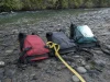 PFD Sizing Guide for Rafters Where Medium Isn’t Medium Three whitewater life jackets laid out on a gravel riverbank next to a soft measuring tape