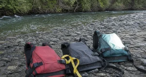 PFD Sizing Guide for Rafters Where Medium Isn’t Medium Three whitewater life jackets laid out on a gravel riverbank next to a soft measuring tape
