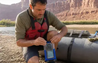 Rafting Electronics Explained by What Survives a Flip Rafter sealing a waterproof phone case on a raft tube before pushing off at the put-in