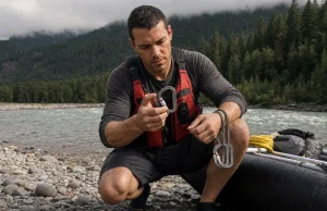 Best River Rescue Carabiners and Pulleys Guides Trust Boater checking river rescue carabiners and pulleys clipped to a raft frame on a gray cobble bar