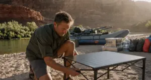 10 Roll-Up Tables and Camp Kitchens Compared You Need Two Rafter setting up a roll-up camp kitchen table on a sandbar beside a rigged oar boat at a river camp