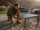 10 Roll-Up Tables and Camp Kitchens Compared You Need Two Rafter setting up a roll-up camp kitchen table on a sandbar beside a rigged oar boat at a river camp