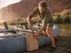 Best Water Jugs for River Trips That Survive a Flip Rafter strapping a Scepter water jug to a raft frame at a desert river put-in before a multi-day trip