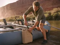 Best Water Jugs for River Trips That Survive a Flip Rafter strapping a Scepter water jug to a raft frame at a desert river put-in before a multi-day trip