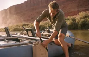 Best Water Jugs for River Trips That Survive a Flip Rafter strapping a Scepter water jug to a raft frame at a desert river put-in before a multi-day trip