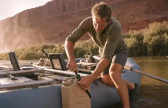 Best Water Jugs for River Trips That Survive a Flip Rafter strapping a Scepter water jug to a raft frame at a desert river put-in before a multi-day trip
