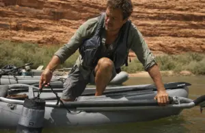 Drag Bags vs Soft Storage for River Camping Loaded mesh drag bag clipped to a raft D-ring, towing alongside the boat on a green desert river