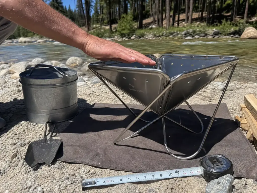 Folding steel fire pan elevated on a sand bar beside a sealed ash can and fire blanket