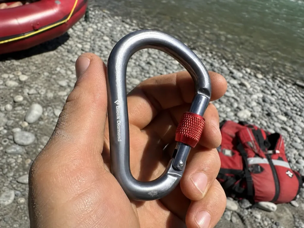 Close-up of a locking carabiner's stamped strength rating held up in harsh midday river light