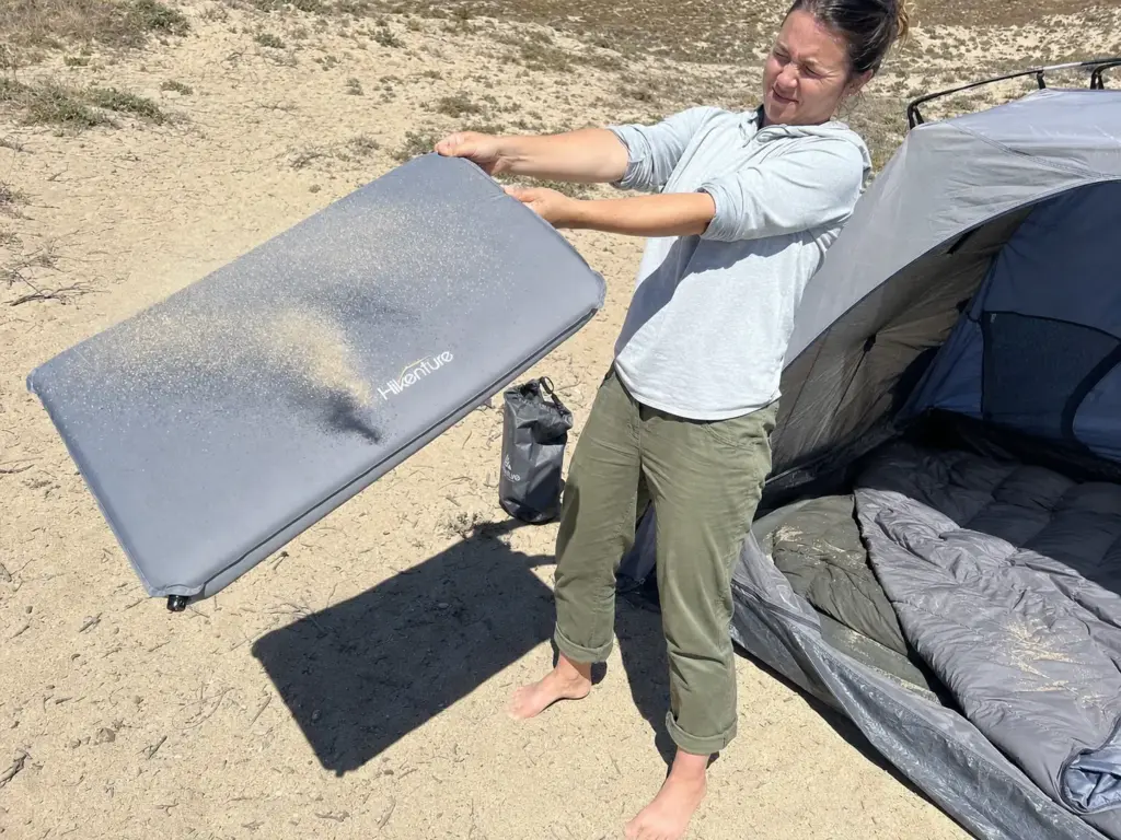 Camper shaking sand out of a sleeping pad on a river sandbar, the classic river camping problem