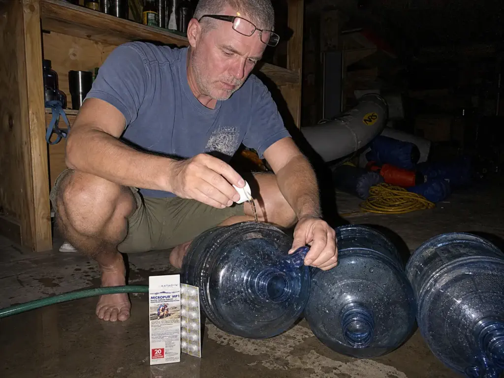 Rinsing and sanitizing river water jugs in a garage before the season with bleach and purification tablets