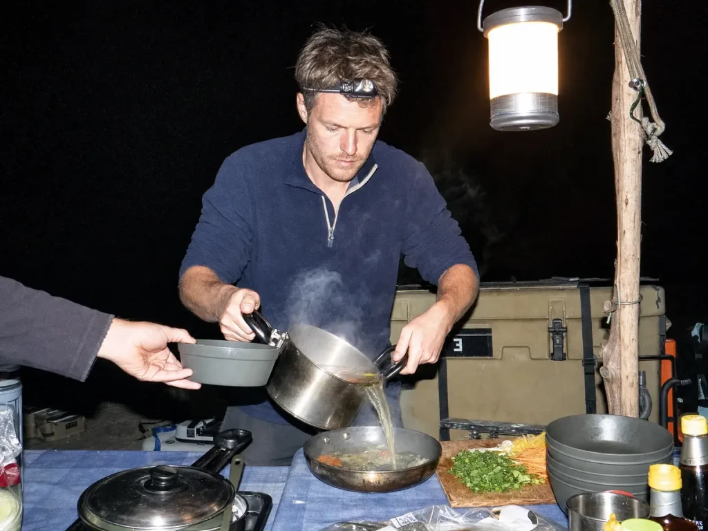 Camp kitchen lit by a hanging lantern instead of headlamps after dark on a river trip
