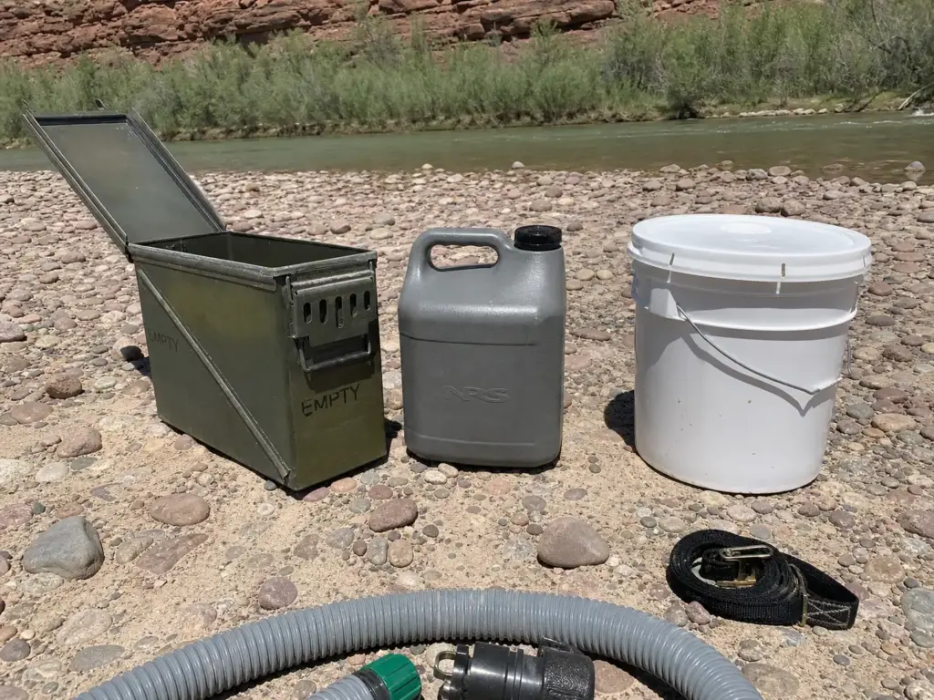 Steel 20mm ammo can beside a rotomolded plastic groover tank laid out on a river gravel bar
