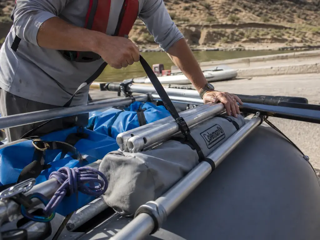 Rolled aluminum roll-top camp table lashed along a raft frame side rail at the put-in