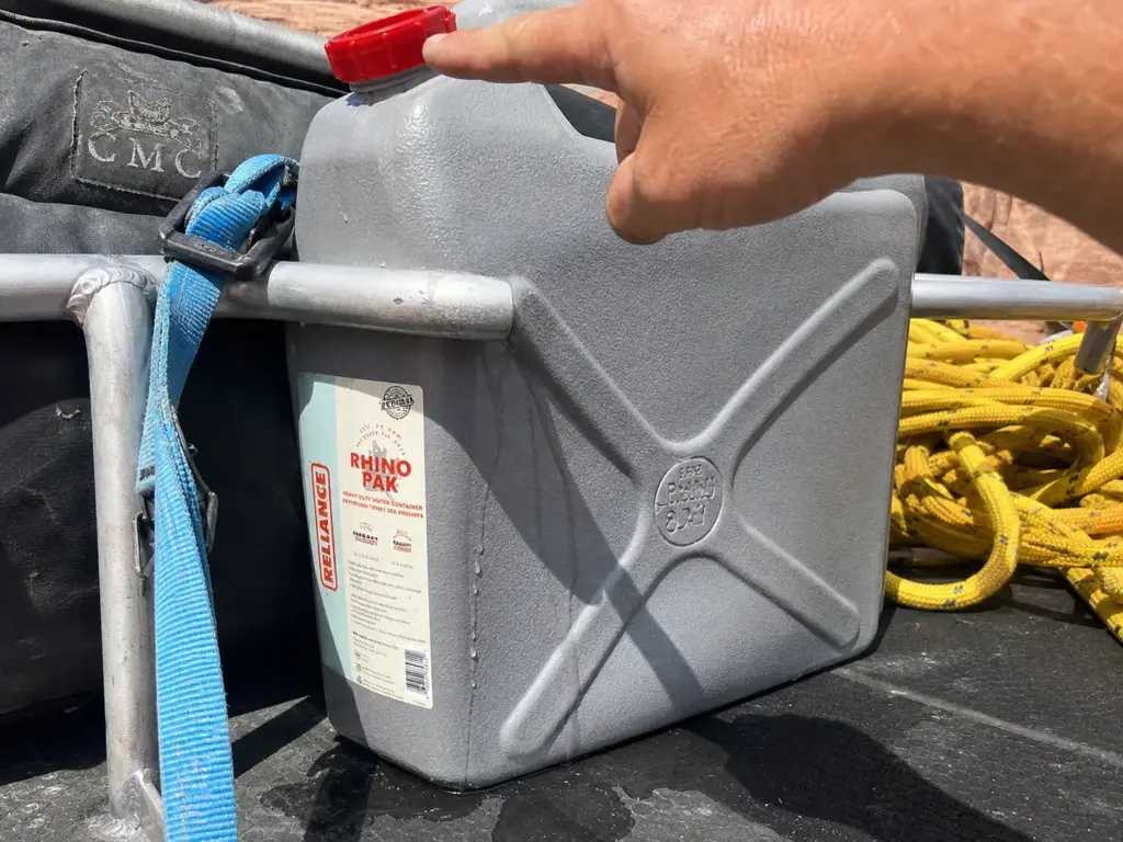 Water jug wedged against a raft frame crossbar showing where the cap and spigot fail on river trips