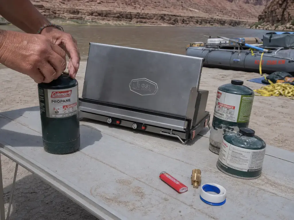 Propane cylinder and canister fuel laid out beside a folding two-burner river camp stove