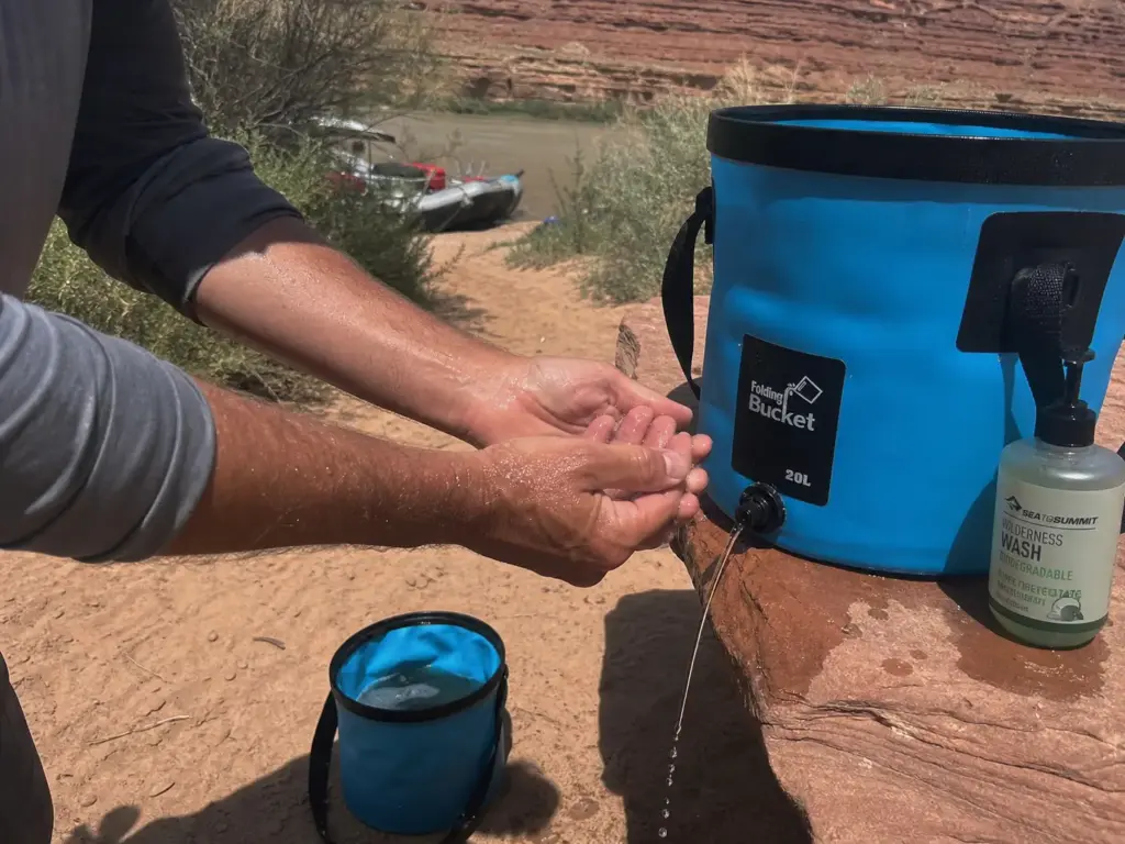 Hands rinsing at a collapsible bucket handwash station on the path back from a river groover