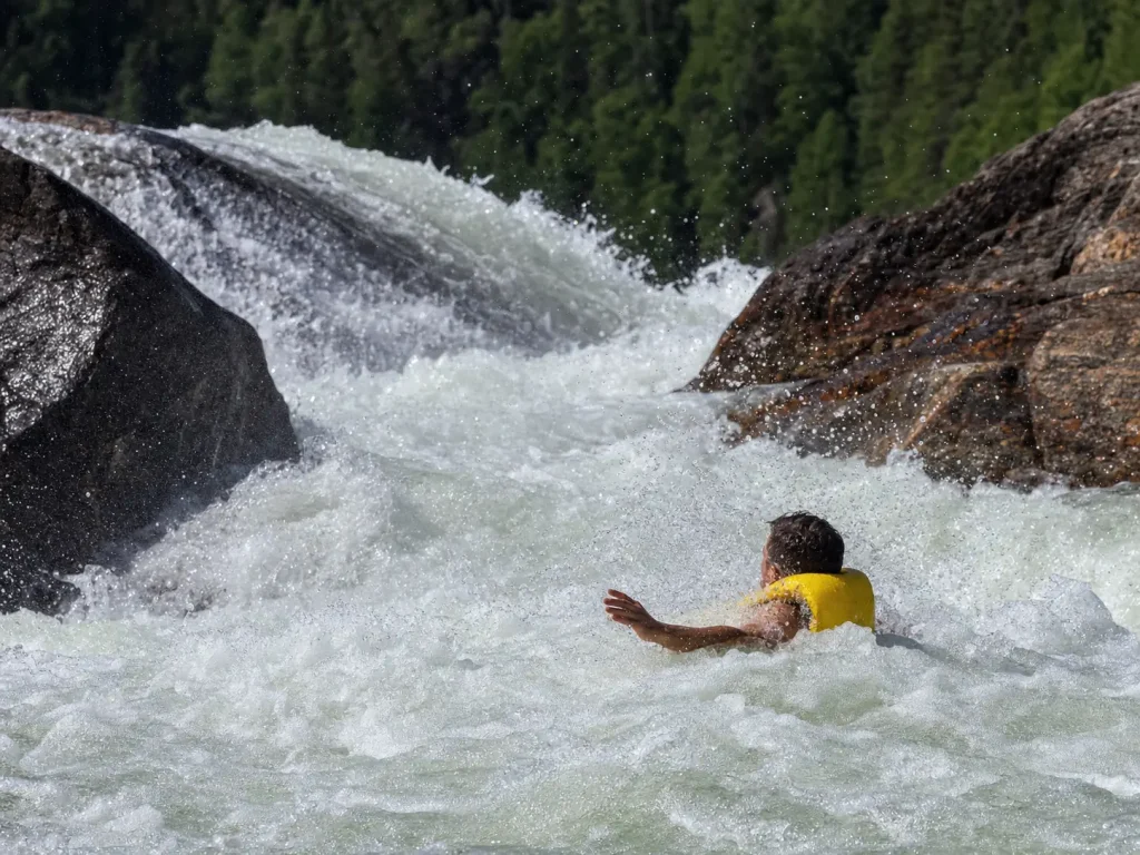 A rafter floating in aerated whitewater with their life jacket holding them high in the foam