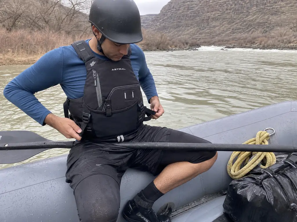 Rafter seated in a raft adjusting the side straps of an Astral Indus rescue PFD for fit