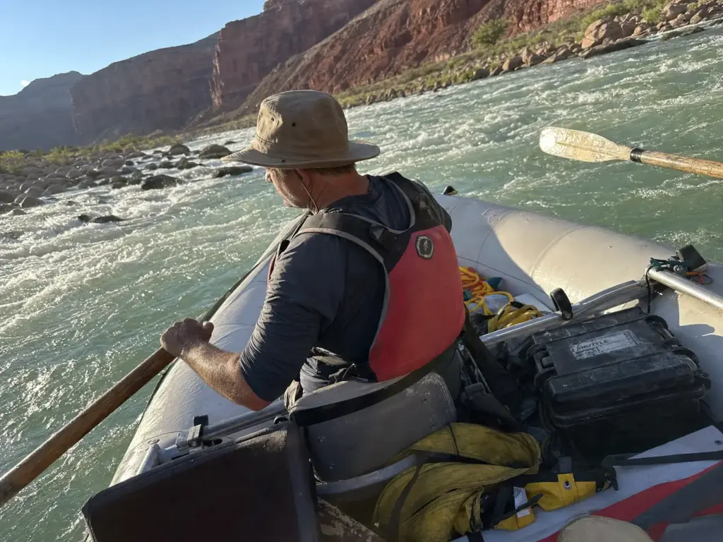 Rower at the oars with a short-tethered drag bag trailing off the stern D-ring of a whitewater raft
