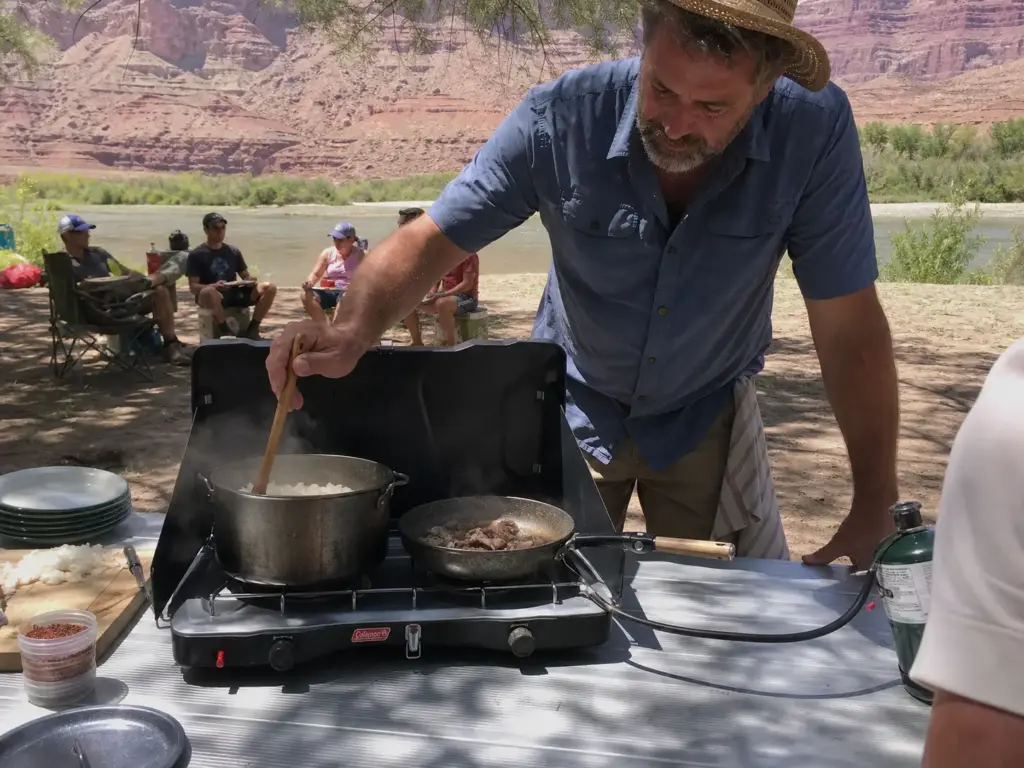 Cooking dinner for a raft crew on a two-burner propane camp stove at a river camp kitchen