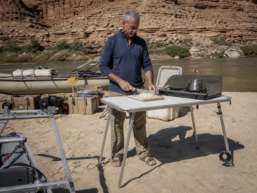 Boater standing at a tall frame-mount river counter set up as a kitchen prep station on a sandbar