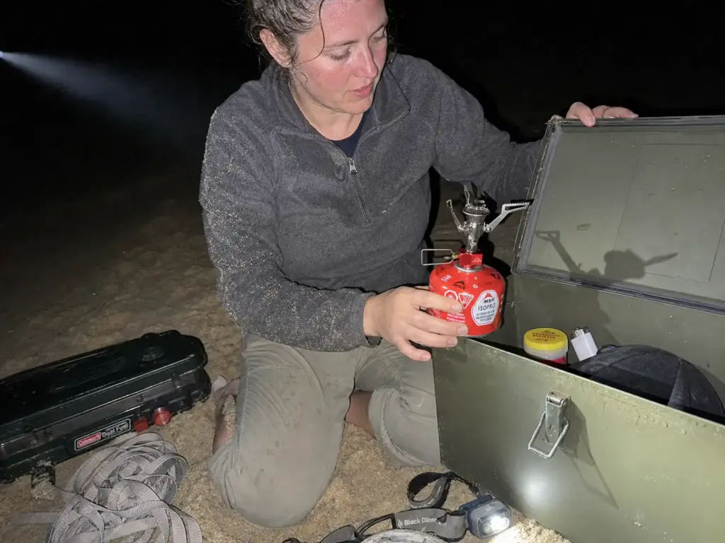 Backup camp stove and stormproof matches sealed into a dry box at a river camp after dark