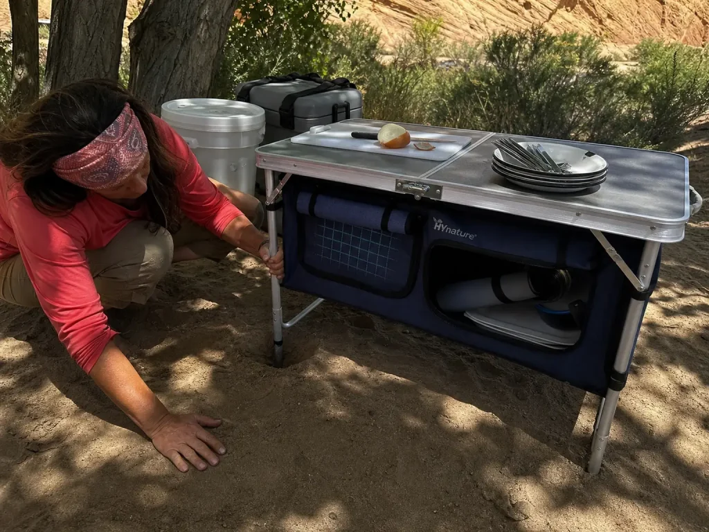 Folding aluminum camp table leveled on uneven sand at a Green River camp kitchen