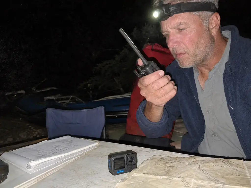 Rafter checking a handheld radio at camp after dark on a multi-day river trip