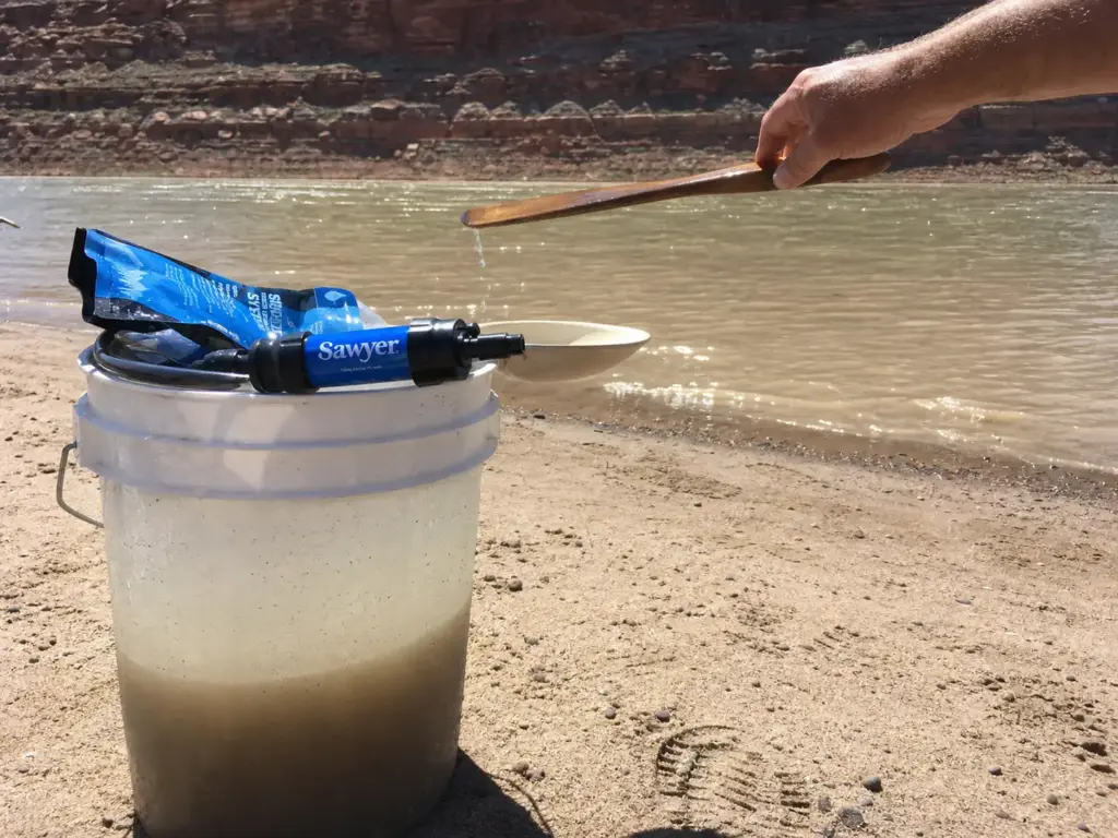 Silty river water settling in a bucket beside a Sawyer Mini filter before treating water on a raft trip