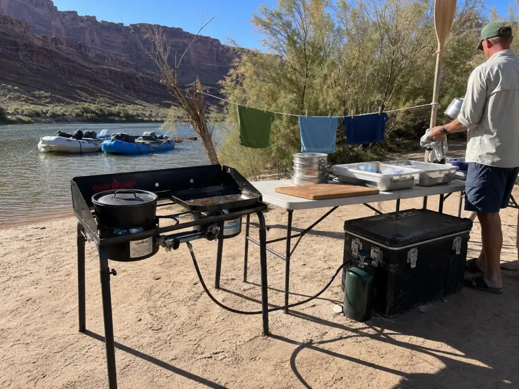 High-output two-burner camp stove set up on legs in a working river camp kitchen line