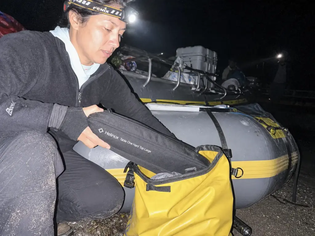 Packed ultralight camp table slid into a dry bag during pre-dawn raft rigging by headlamp